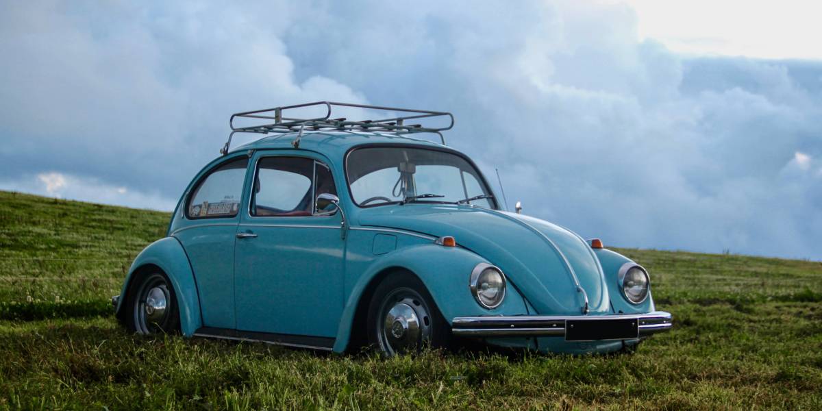 Abgemeldetes Auto VW Käfer in himmelblau ohne Kennzeichen auf grüner Wiese. Im Hintergrund Wolken