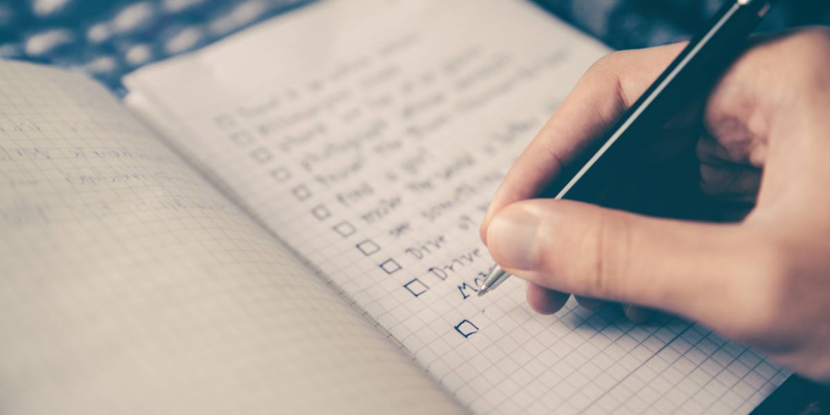 Seite eines Notizbuches mit einer Checkliste Autoverkauf. Rechte Hand mit schwarzem Stift in Schreibhaltung.