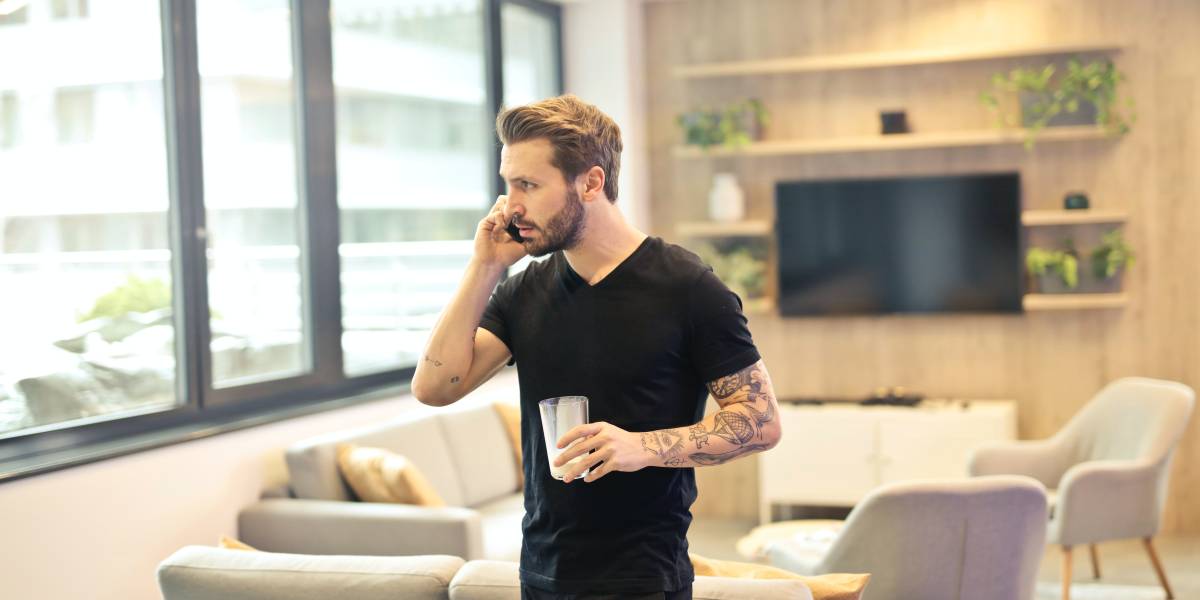 Junger Mann telefoniert im Wohnzimmer mit Handy. Informiert sich über KFZ-Ankauf